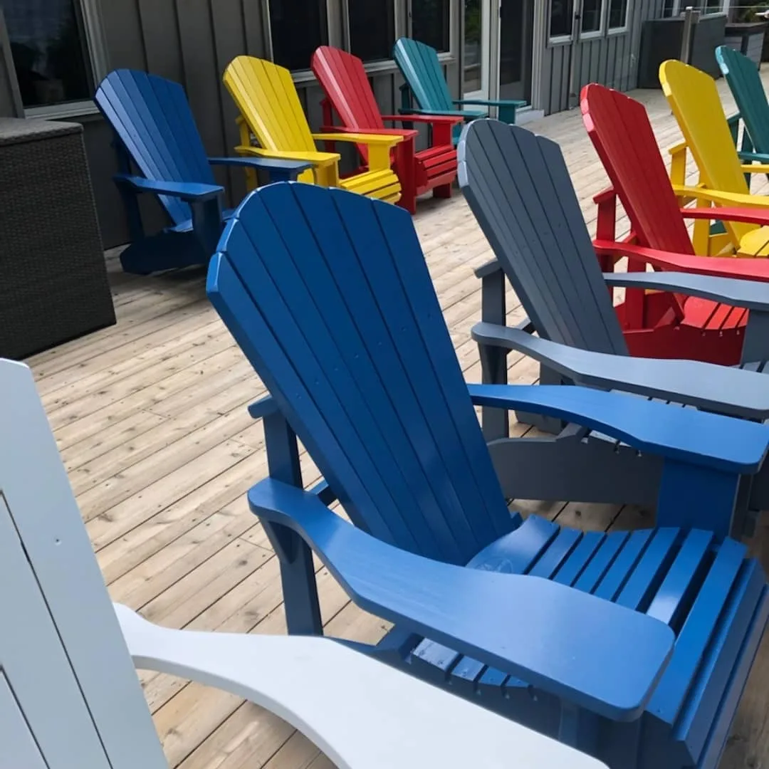 Multi-colored Adirondack chairs painted in vibrant primary colors on a wooden deck, demonstrating TAG's premium offsite spraying services